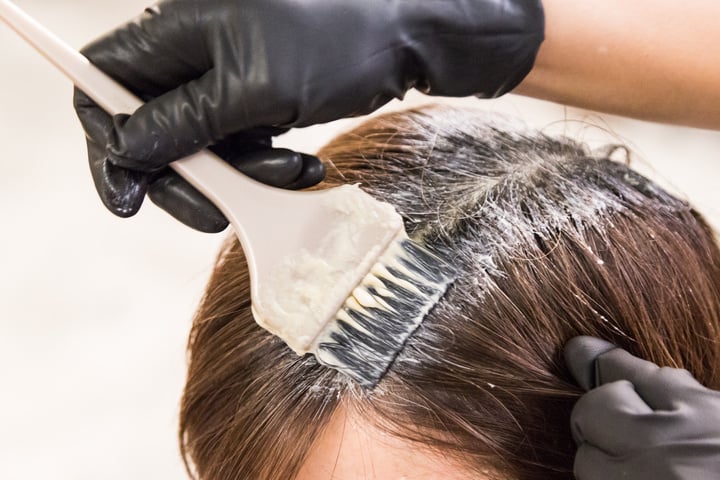 Closeup of hair dresser applying chemical color dye onto hair